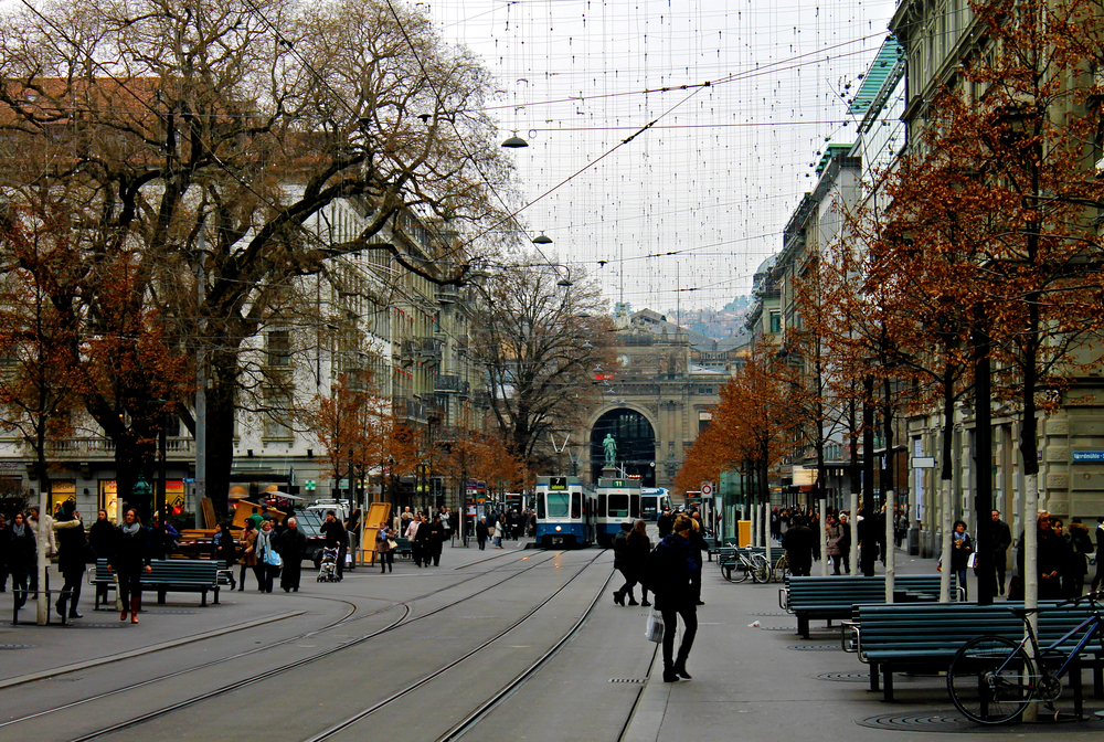 Bahnhofstrasse em Zurique com trilhos de bonde, pedestres e a estação central no fim da rua