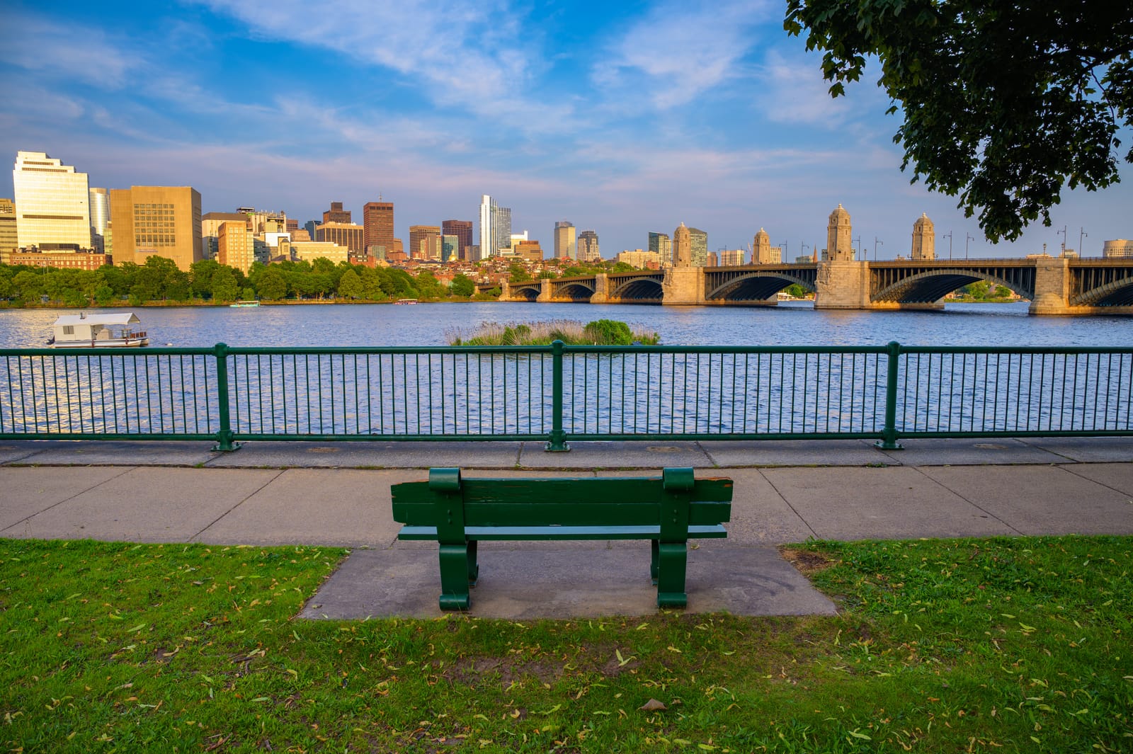 Banco à beira do rio Charles com o skyline de Boston e uma ponte ao fundo
