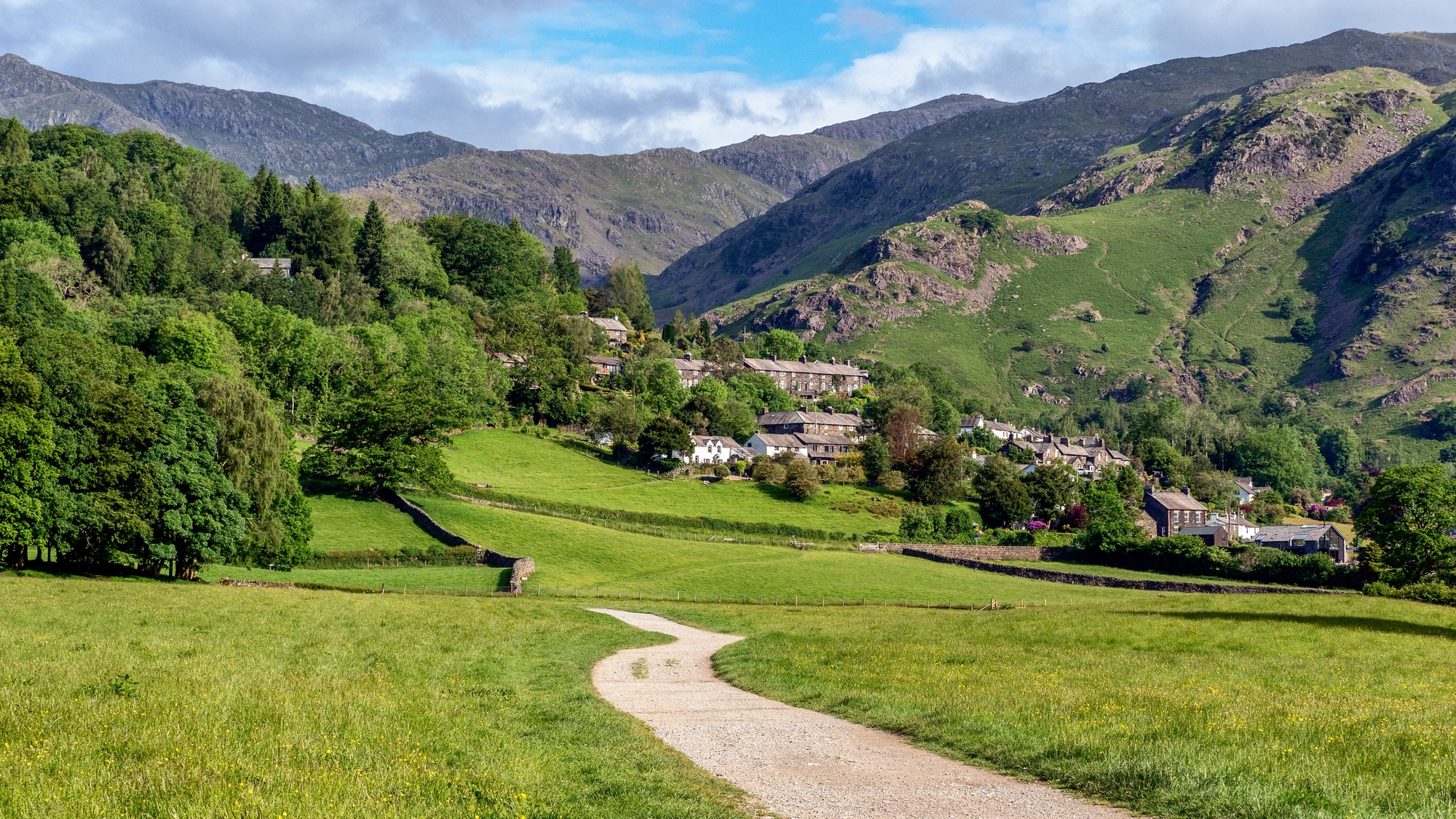 Caminho por um campo gramado em direção ao vilarejo de Coniston, com colinas ao fundo