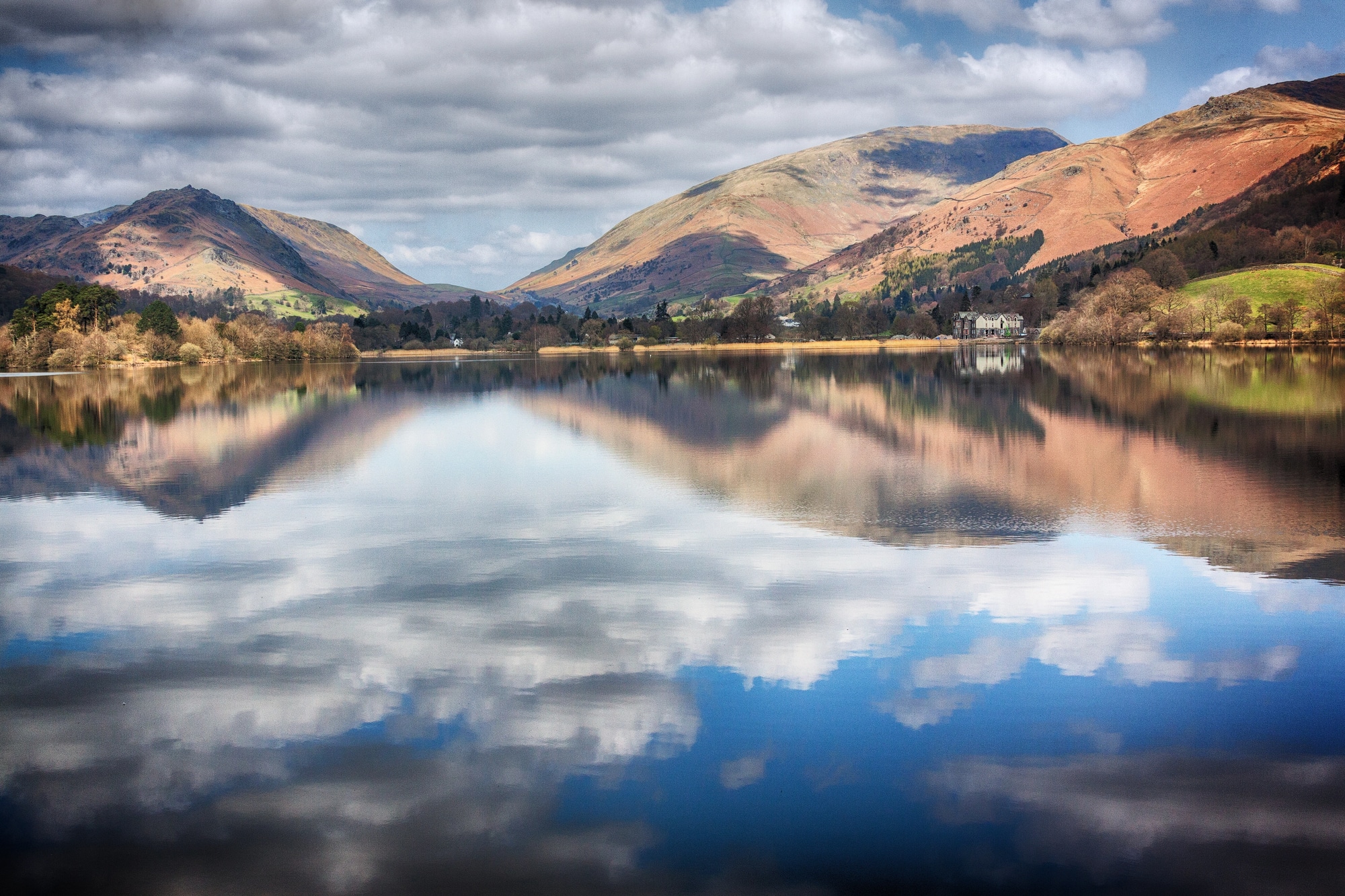Colinas outonais e nuvens refletidas nas águas calmas de Grasmere
