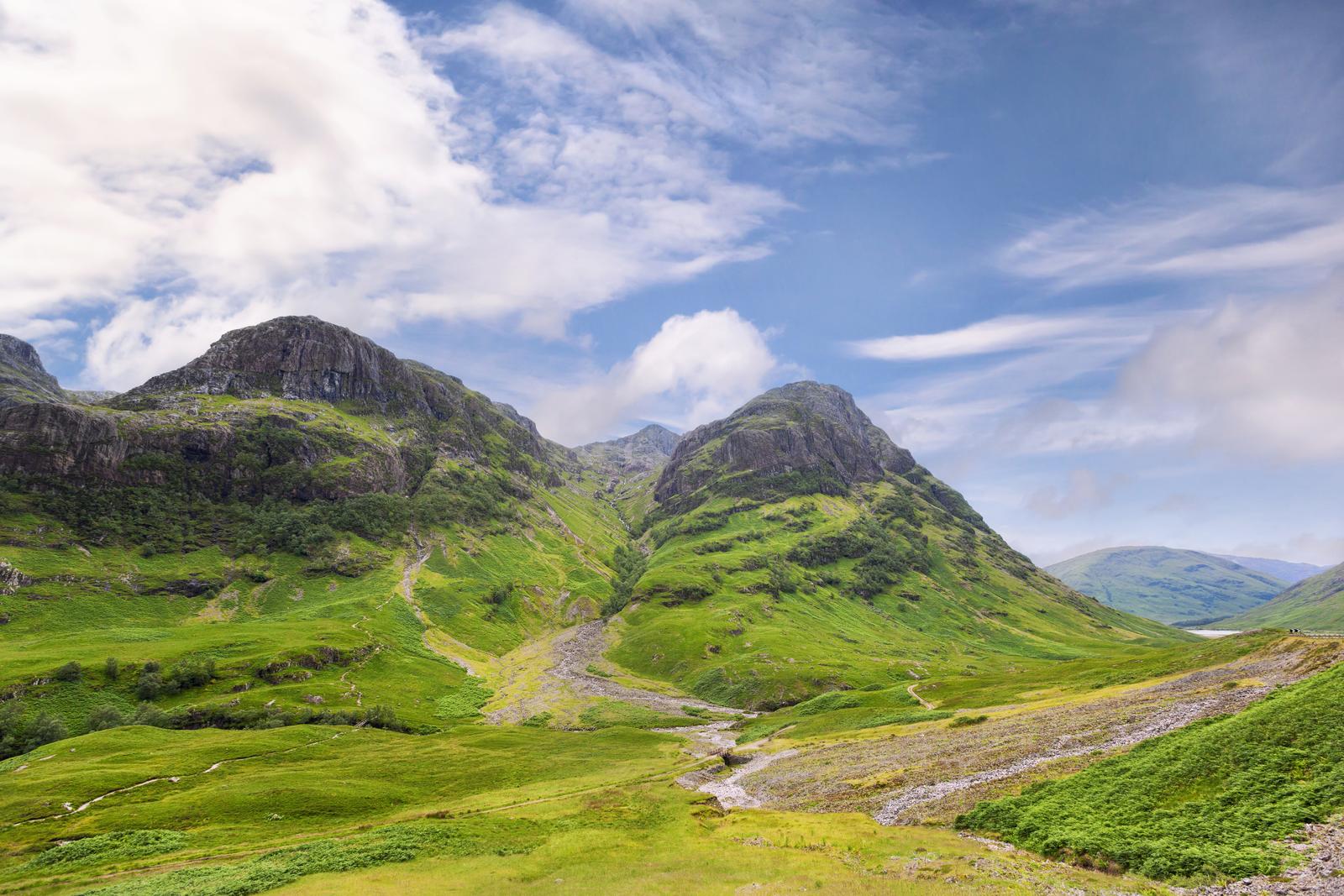 Encostas verdes e uma estrada no vale abaixo das Three Sisters de Glencoe