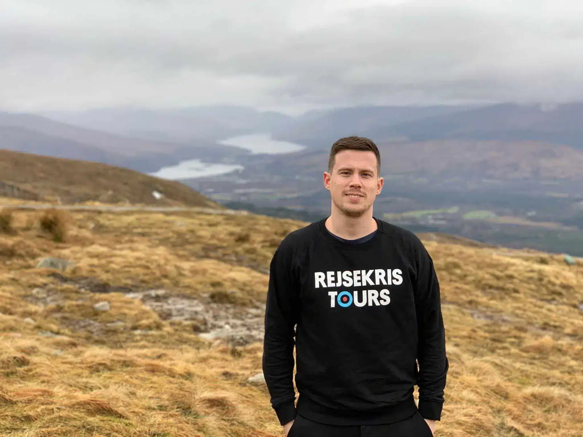 Kristoffer Fons, do Destination Well Known, numa encosta gramada com montanhas ao longe perto de Fort William