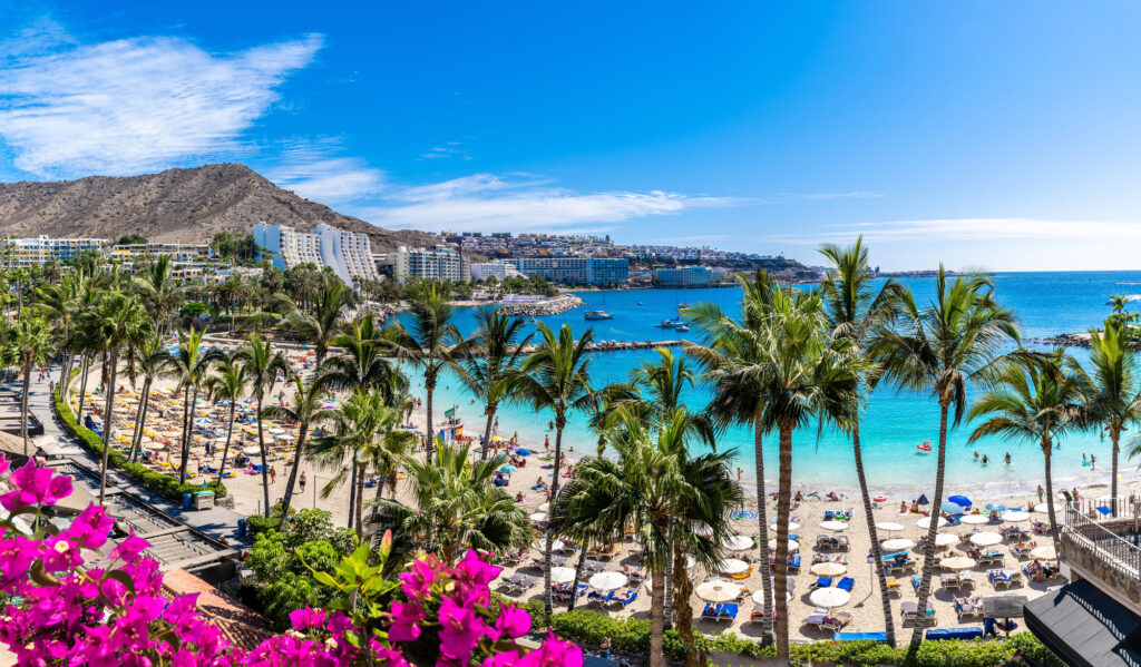 A praia de Anfi del Mar, em Gran Canaria, com palmeiras, guarda-sóis e água azul-turquesa