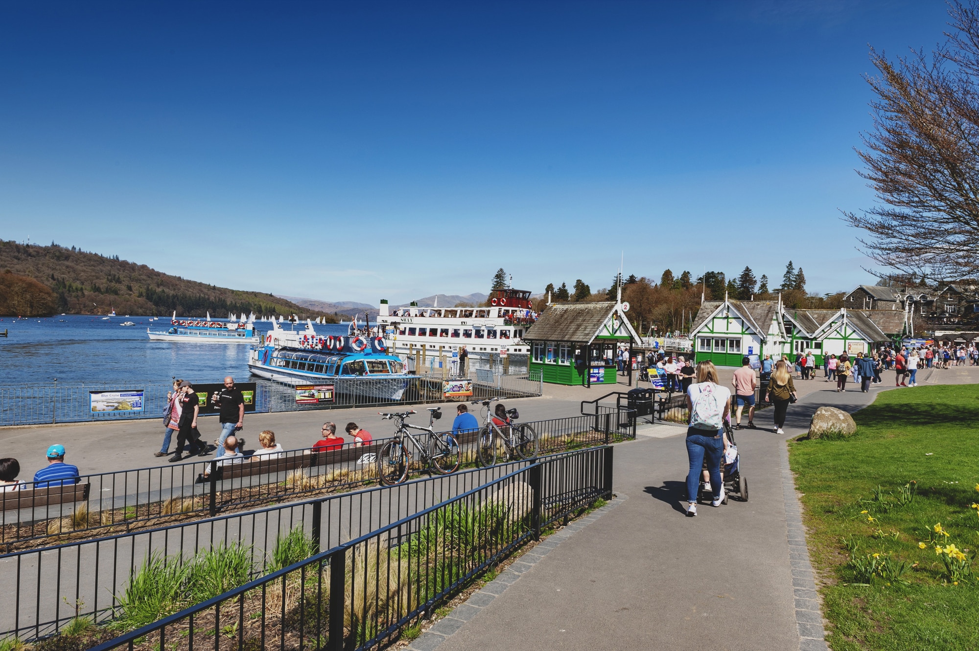 Pessoas caminhando pela orla de Bowness-on-Windermere com um barco no lago