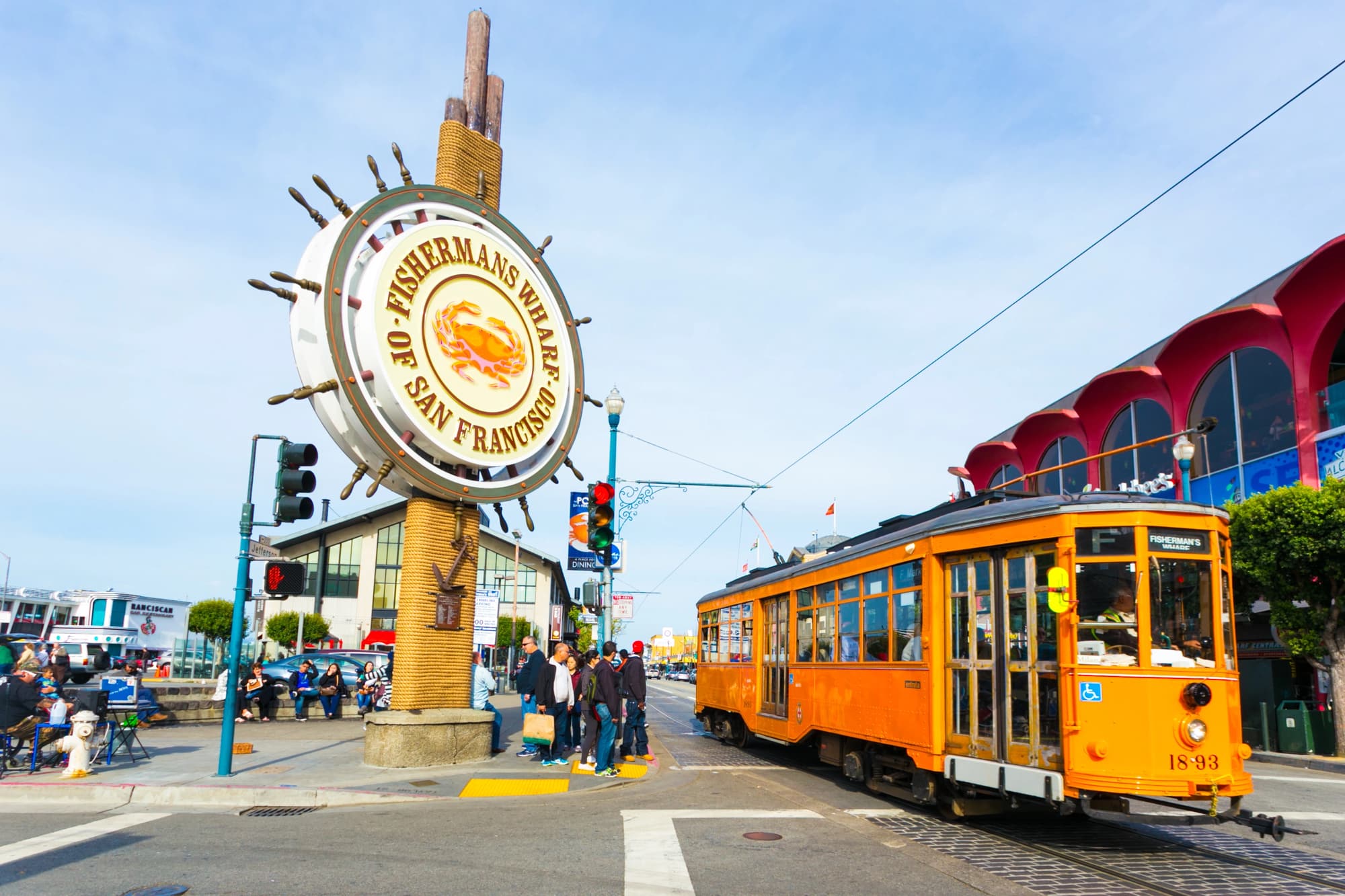 Placa de Fisherman’s Wharf ao lado de um bonde laranja e de prédios da orla