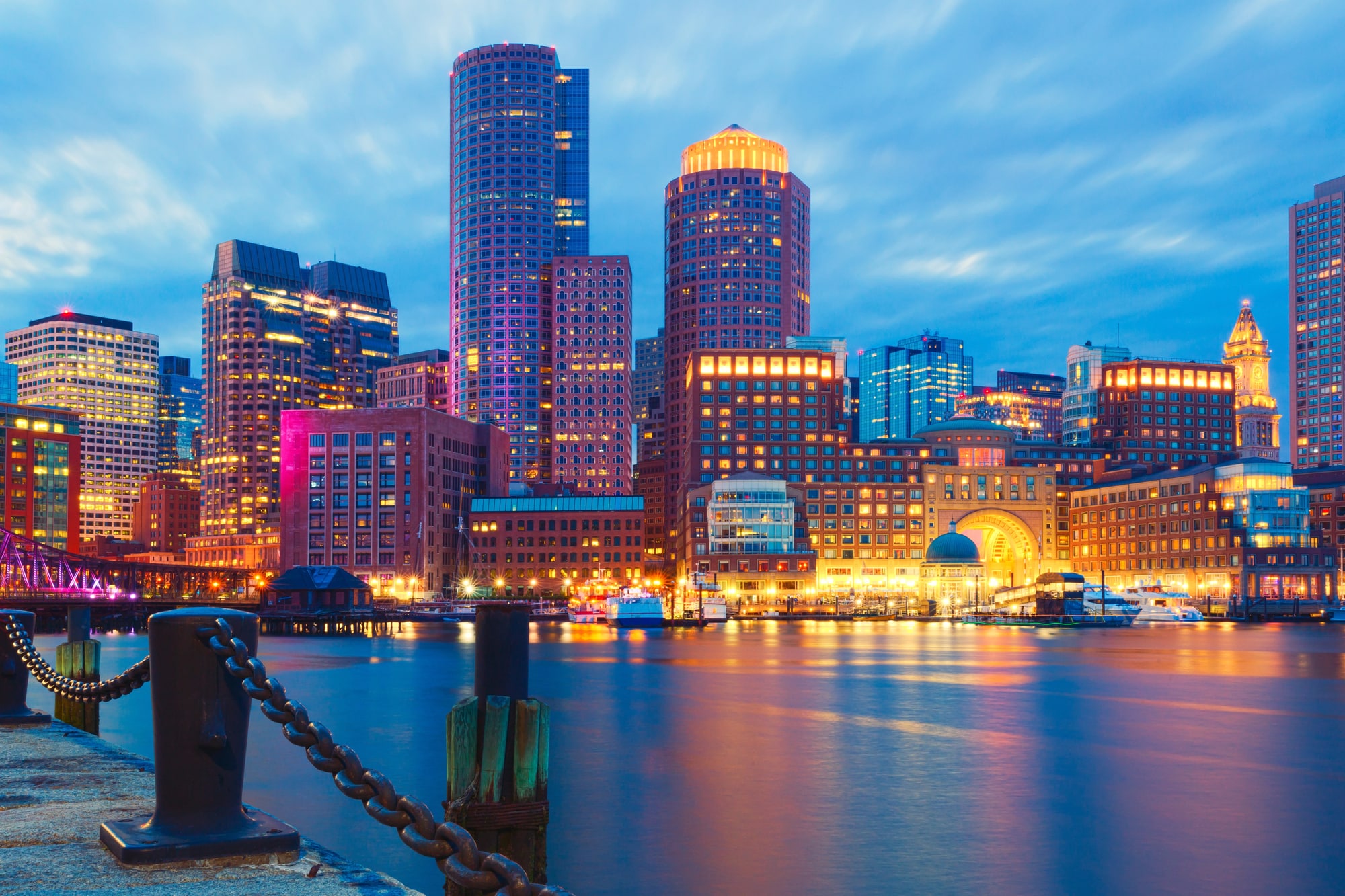 Prédios iluminados ao longo da orla de Boston refletidos na água ao entardecer