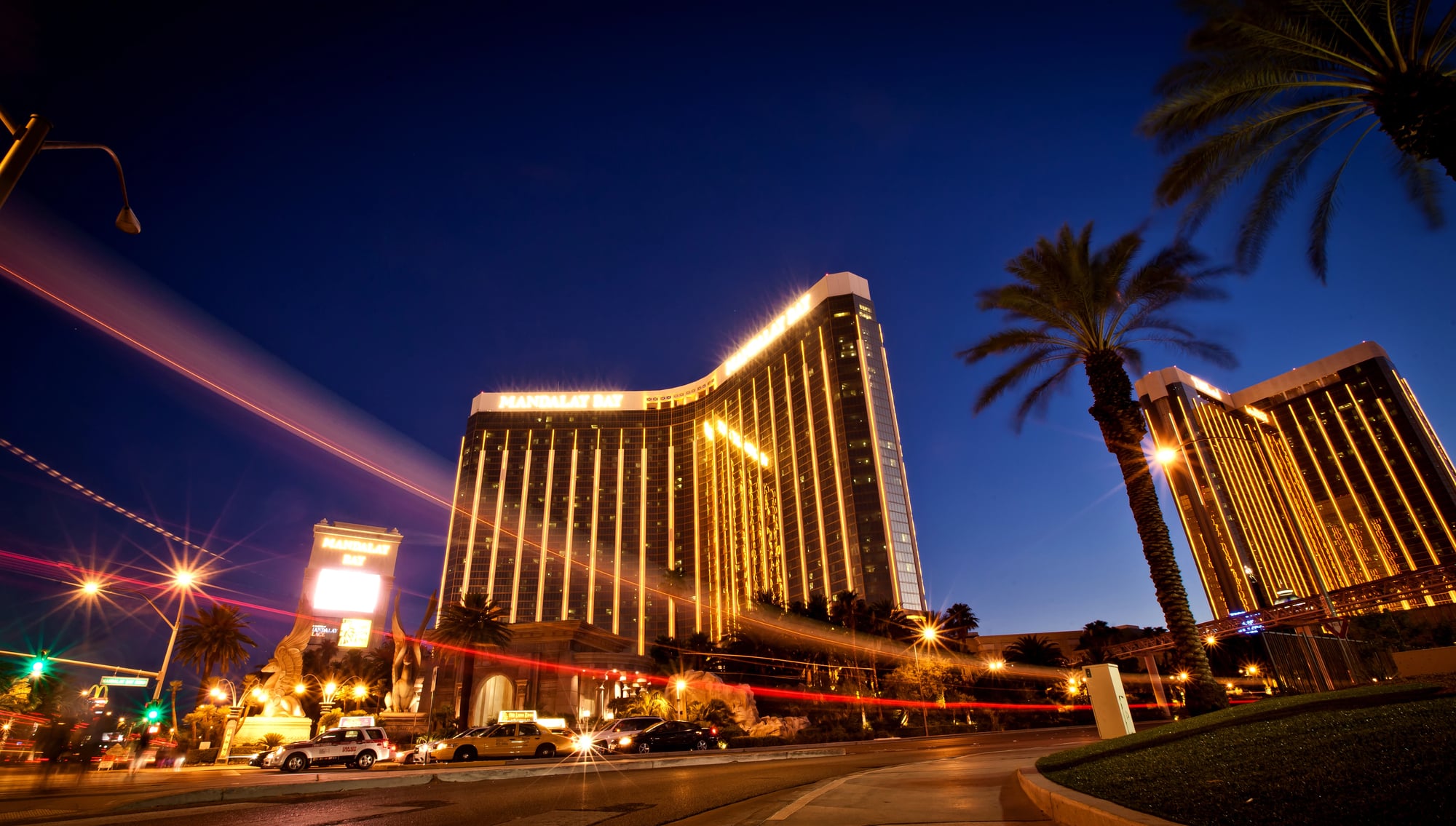 Torre do Mandalay Bay iluminada, com palmeiras e carros passando à noite