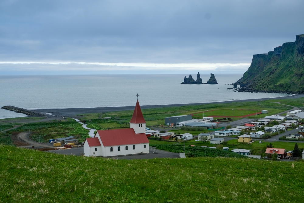 Vík com sua igreja, a praia de areia preta e as formações rochosas de Reynisdrangar na Costa Sul da Islândia