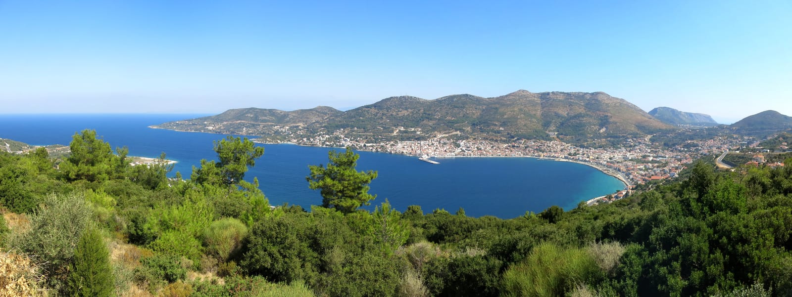 Vista ampla de uma baía em Samos com encostas arborizadas e construções ao longo da costa